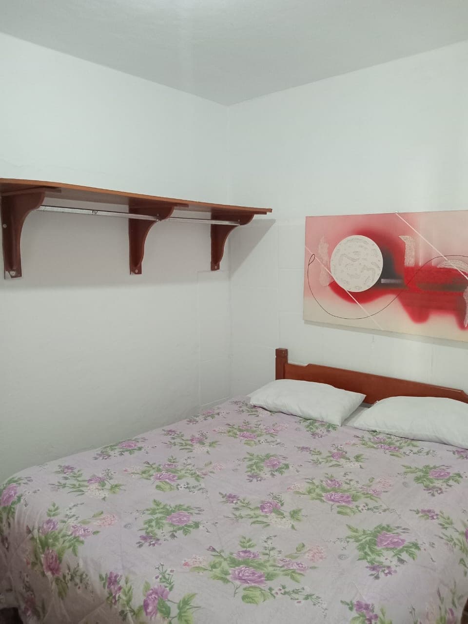 Quarto com cama floral clara e prateleira de madeira